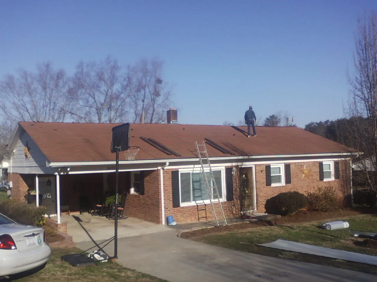 Roofer stripping a shingle roof on a brick ranch before metal panels in Potsdam