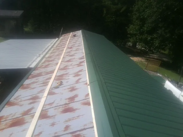 Old rusted panels beside newly installed green metal roofing — Wind Damage Roof Repair by Roofing Brothers in Potsdam